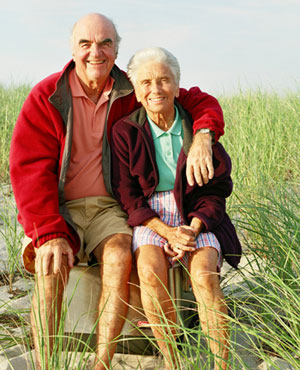Elderly couple smiling and hugging outdoors in dunegrass landscape.